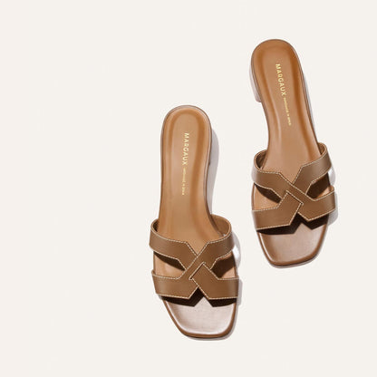 The MX 35 - Mocha Calf by Margaux features tan slide sandals with open toes, crisscross straps, white stitching, and the Margaux name in gold on the insole—all displayed on a plain white background for a chic, walkable look.