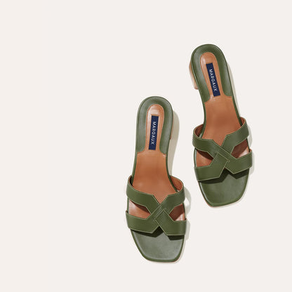 The MX 35 - Olive Calf by margaux-development: olive green slip-on sandals with crisscross leather straps, tan insoles, and dark blue MARGAUX labels, shown on a light beige background—an elevated classic.