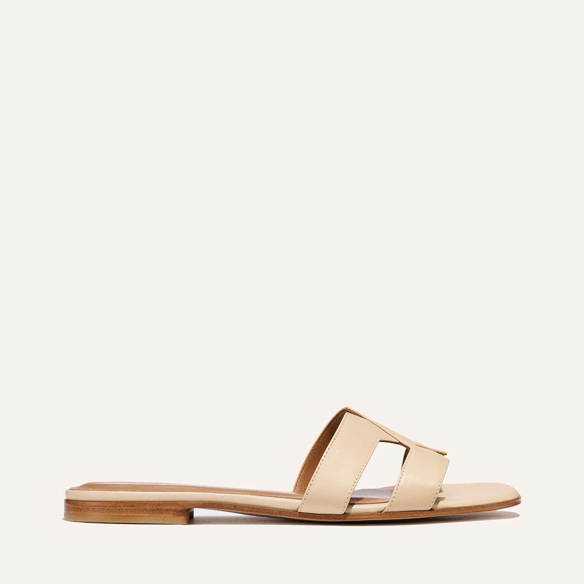 The Margaux MX Sandal in Latte Calf features luxe beige leather, an open toe, wide cut-out strap, and low wooden sole—your go-to elevated everyday flat, shown on a plain light background.
