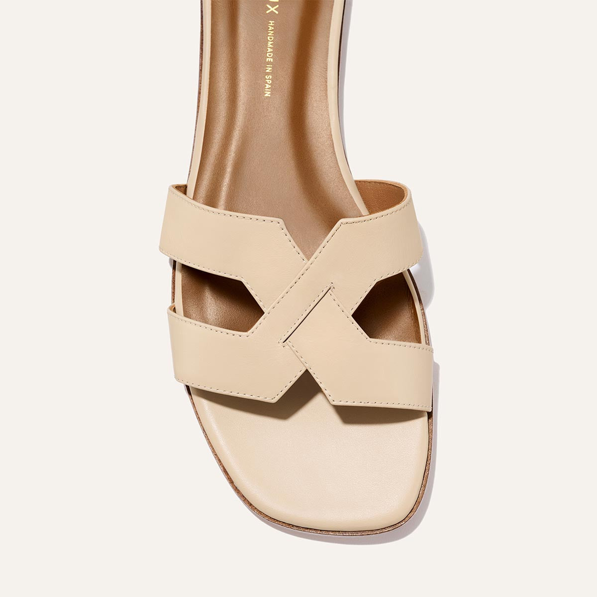 A close-up of Margaux’s The MX Sandal in Latte Calf, featuring luxe leather, a square toe, and crisscross cutout straps on a light background—ideal for elevating your everyday style.
