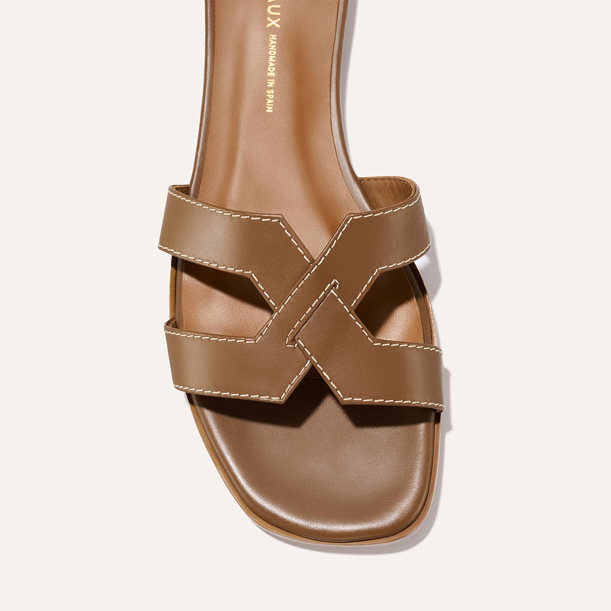 The MX Sandal - Mocha Calf by Margaux features a brown flat design with two wide crisscross straps, white stitching, a square toe, and a smooth, slightly padded footbed. The Margaux brand name is subtly printed on the insole.
