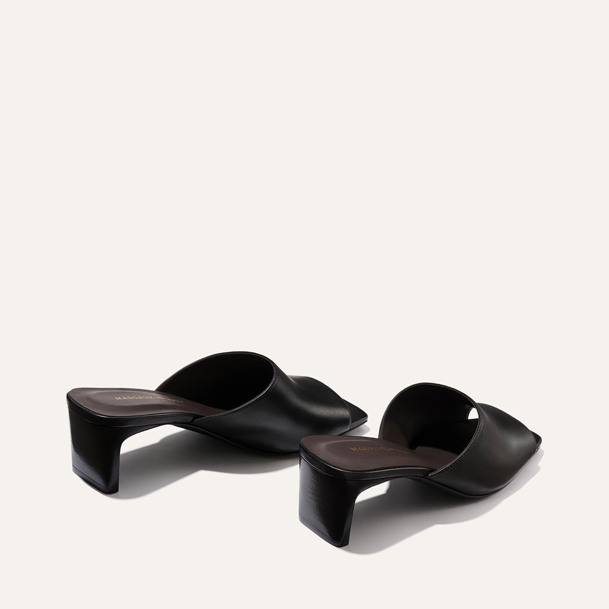 Margaux's The Naomi 50 in Black Nappa: black open-toe slip-on heeled sandals with wide crossed leather straps and chunky square block heels, displayed on a light beige background.