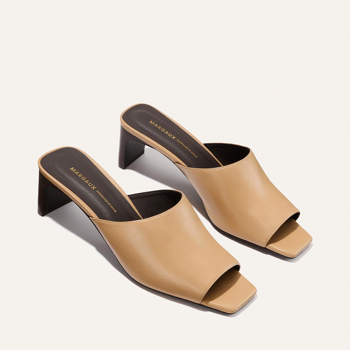 Pair of beige high-heeled mules on a light gray background