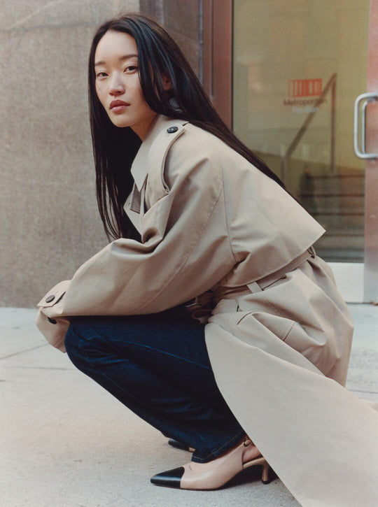 Woman in a beige trench coat squatting on a sidewalk