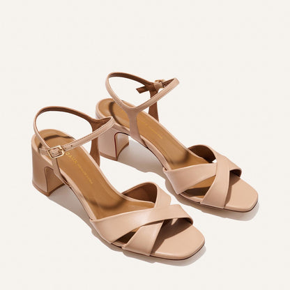 The Paloma Sandal - Dune Nappa by Margaux features beige open-toe block heels with crisscross toe straps and ankle buckles, displayed on a simple light background.