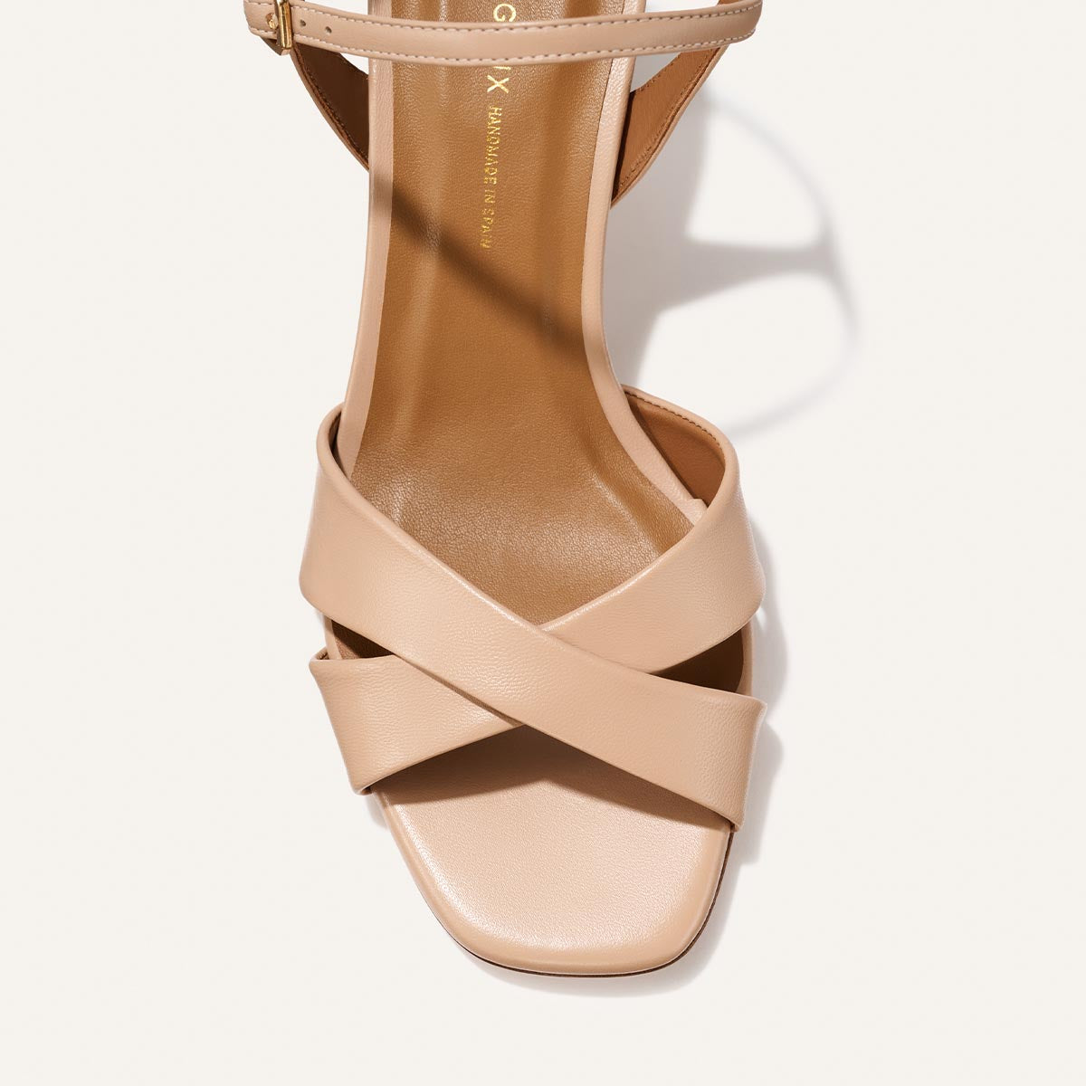 A close-up top view of Margaux’s The Paloma Sandal in Dune Nappa, featuring beige crisscross straps and a square-shaped open toe design against a light background.