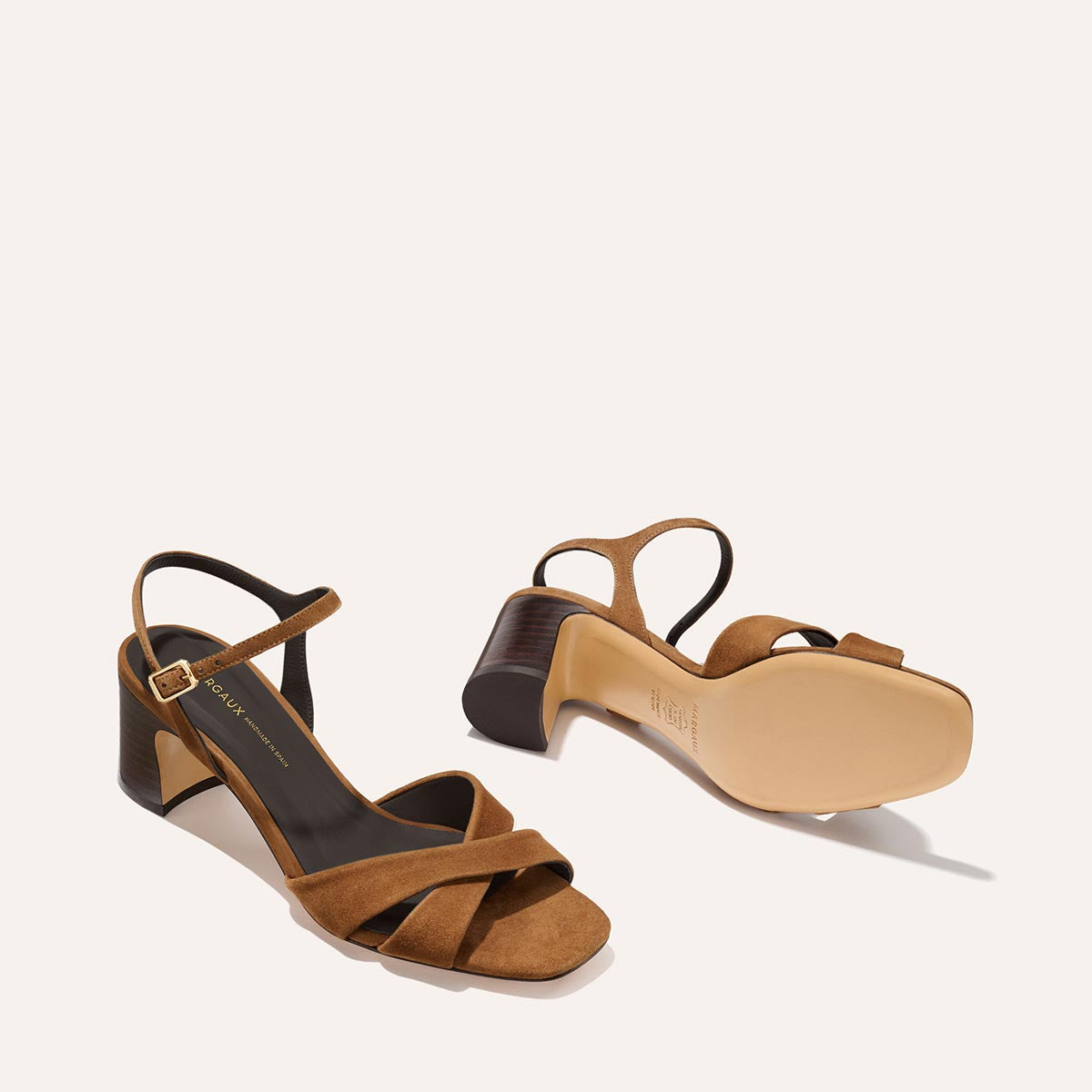 The Paloma Sandal in Nutmeg Suede by Margaux features 2.5-inch block heels and crisscross leather straps; one sandal stands upright, the other shows the sole, both displayed on a light background—your perfect everyday choice.