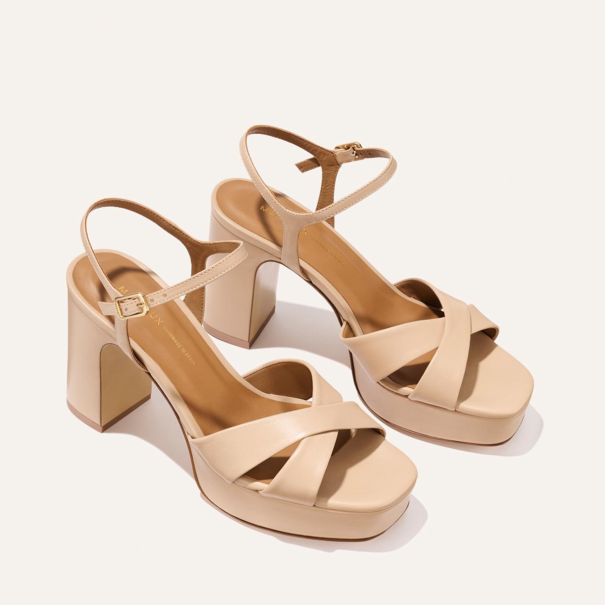 The Margaux Paloma Platform in Dune Nappa features beige chunky heels, crisscross straps, a cushioned platform for all-night comfort, ankle straps with buckles, and an open toe—all shown on a light background.
