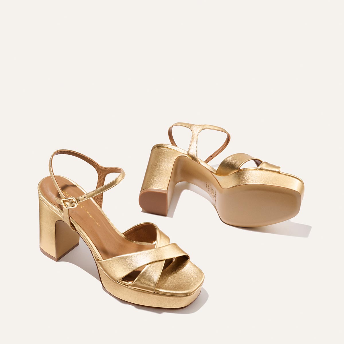 The Paloma Platform - Gold Nappa by Margaux features comfy straps and crisscross toe bands. Displayed on a light background, one sandal stands upright while the other lies on its side, showing the padded platform sole.