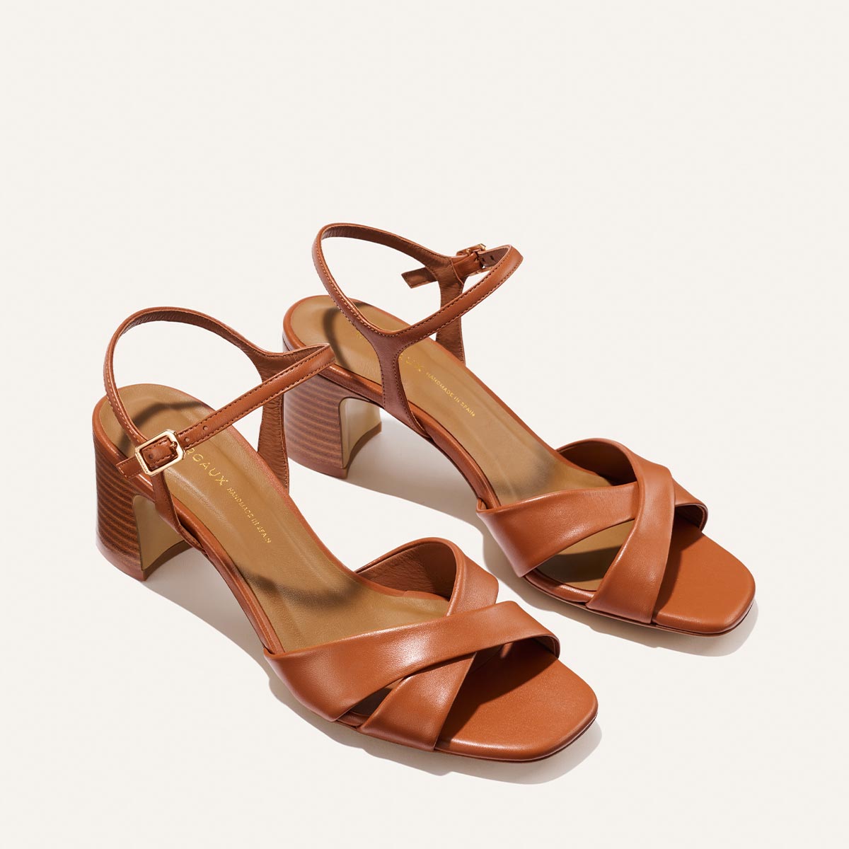 The Paloma Sandal - Saddle Nappa by Margaux features brown crisscross front straps, an ankle strap with buckle, and a block heel, shown on a plain light background.