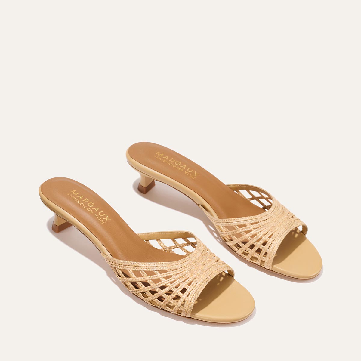 Pair of beige high-heeled sandals with woven design on a white background
