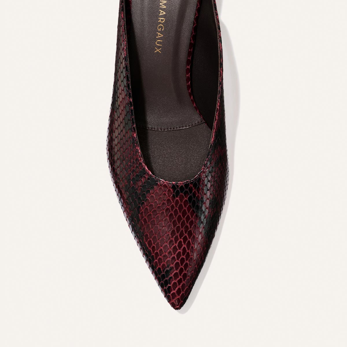 Close-up of the Margaux Alison Roman x Margaux: The Parlor Mule - Burgundy Python Embossed, featuring a pointed toe, burgundy and black python-embossed pattern, and a dark insole, photographed on a light background.