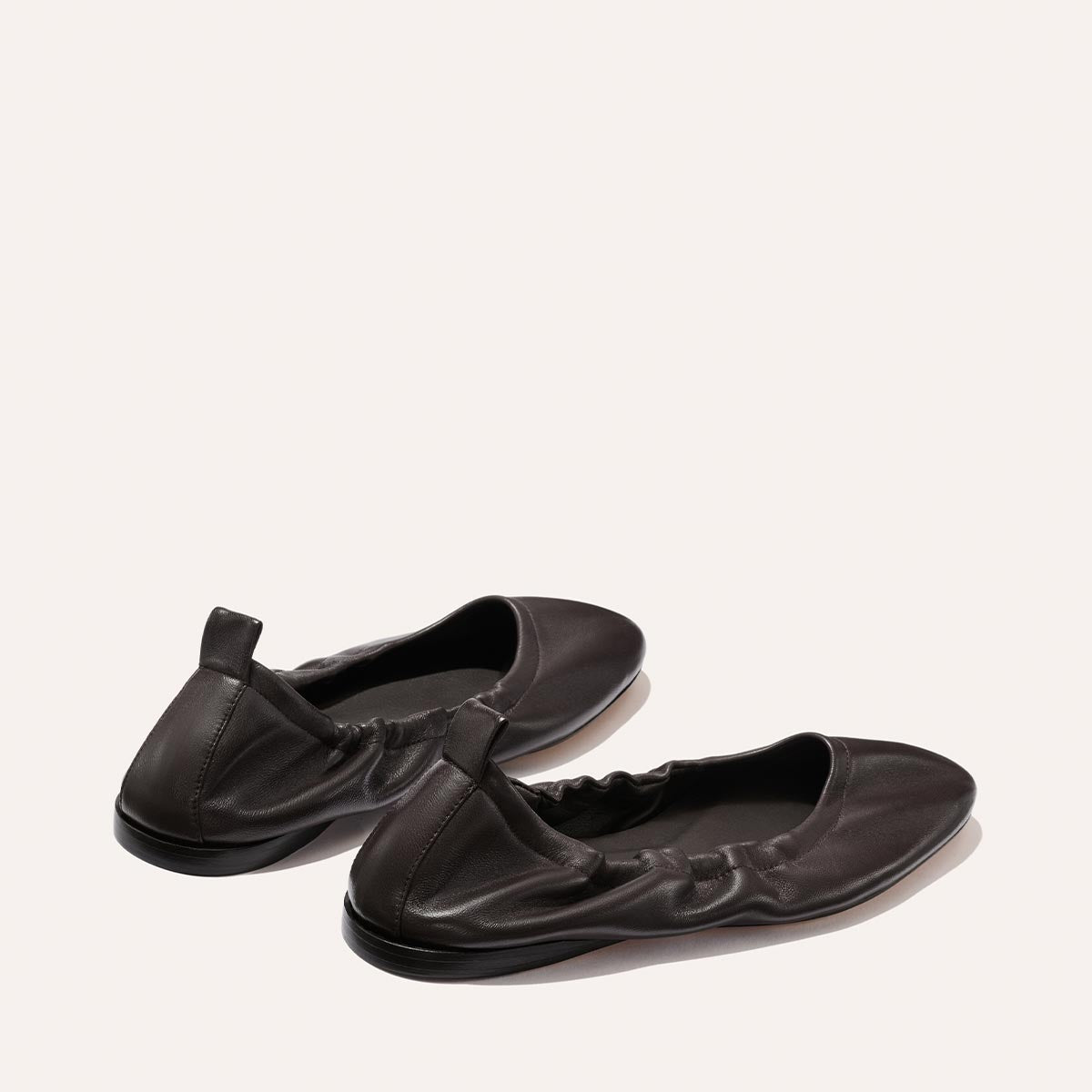 A pair of The Pascale - Espresso Nappa ballet flats by Margaux, crafted from supple dark brown leather with elastic side detailing and small pull tabs at the heels, displayed on a plain light background.