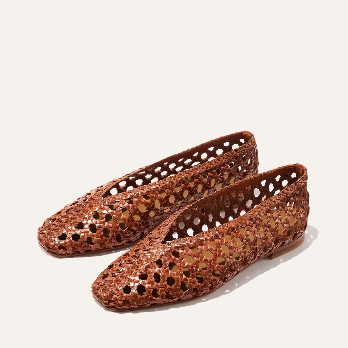 The Woven Paz - Saddle Leather by Margaux: a pair of brown handwoven flats with a geometric cut-out pattern and soft finish, shown against a plain white background.