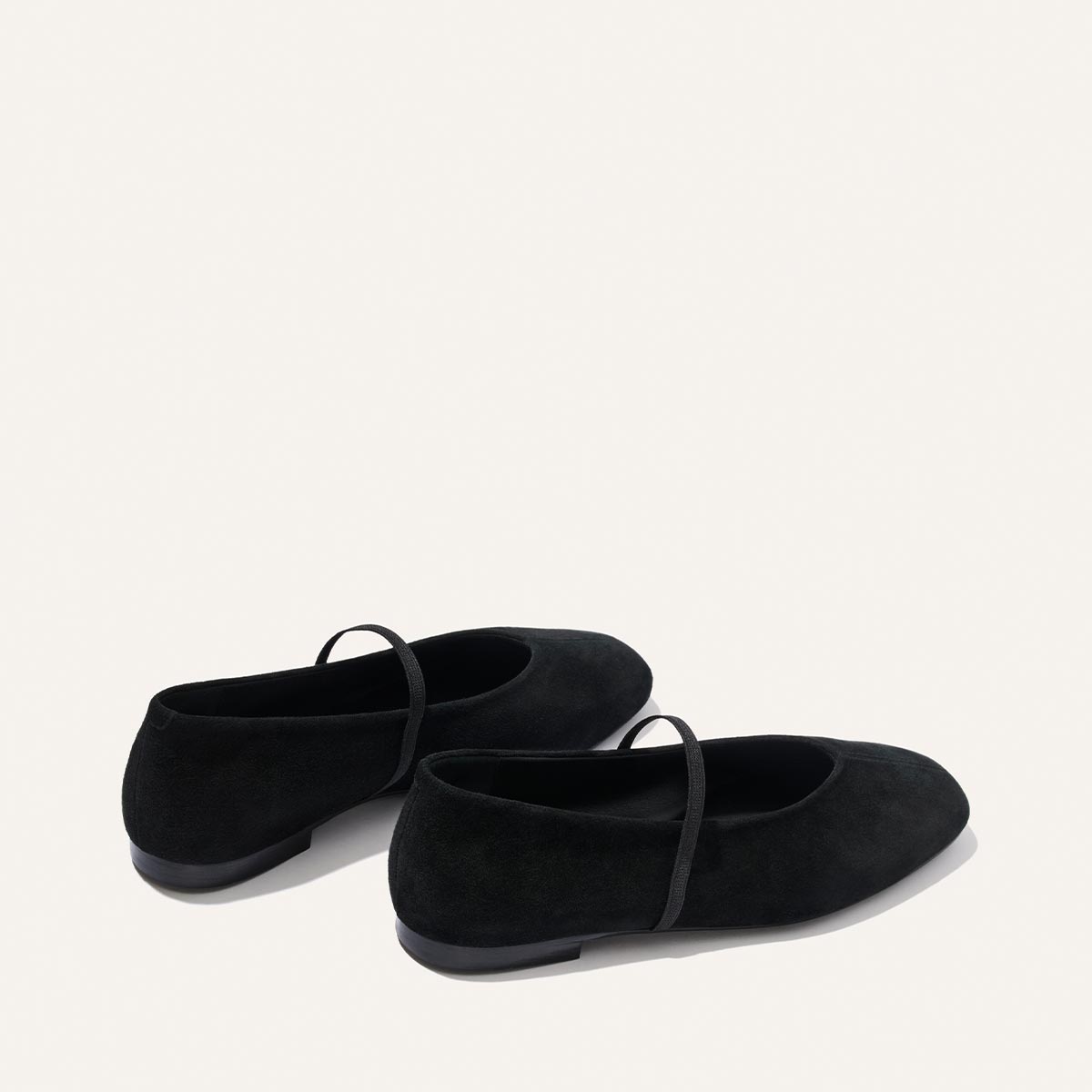 A pair of The Phoebe - Black Suede Mary Jane flats by Margaux, featuring thin straps and displayed on a plain white background.