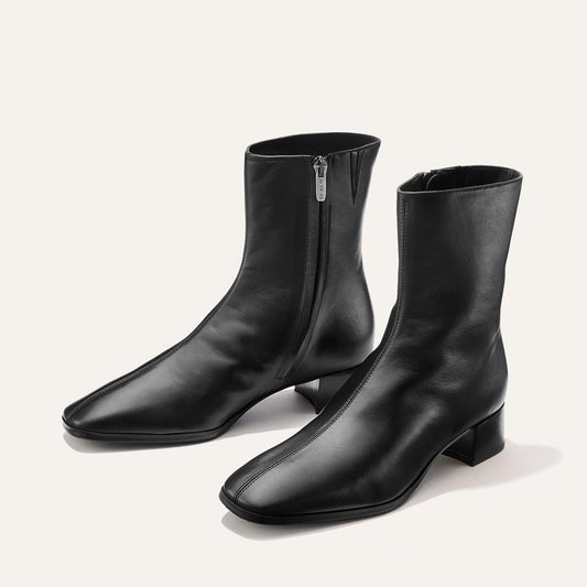 The Phoebe Boot - Black Calf by Margaux is a pair of black leather ankle boots with a side zipper, low block heels, and a subtly squared toe, crafted using the artisanal sacchetto technique and finished with a padded insole for exceptional comfort. Shown on a light background.