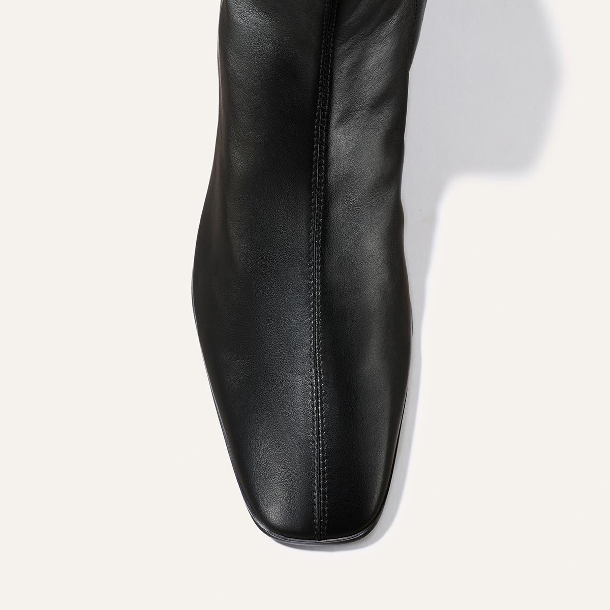 Top view of The Phoebe Boot by Margaux in black calf leather, showcasing a square toe and prominent central seam against a light background. Crafted with the artisanal sacchetto technique, this comfortable flat features a padded insole for enhanced comfort.