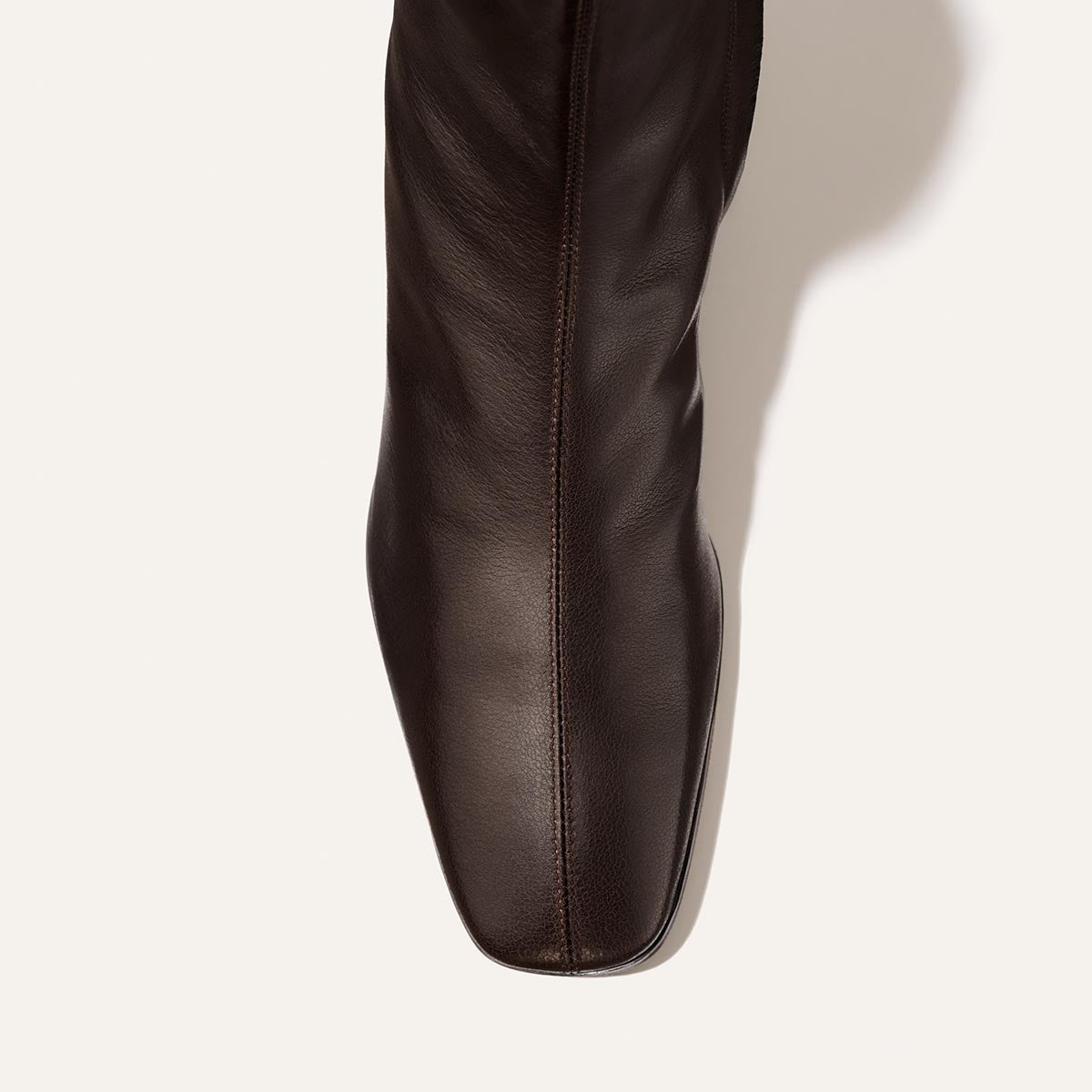 A top view of the Margaux Phoebe Boot in Dark Chocolate Calf showcases its square toe, center stitching, and a subtle shadow on a white background. Featuring a padded insole for enhanced comfort, this boot combines timeless style with all-day support.