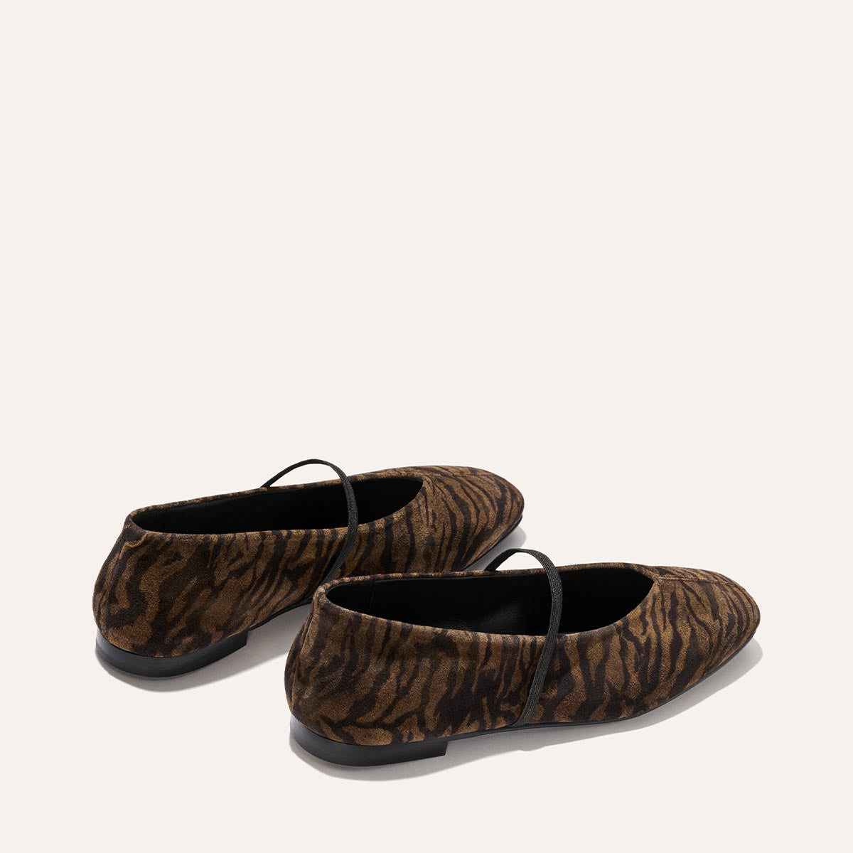 The Phoebe - Brown Zebra Suede flats by Margaux feature brown and black zebra stripes with black straps, shown from a rear side angle on a light background.