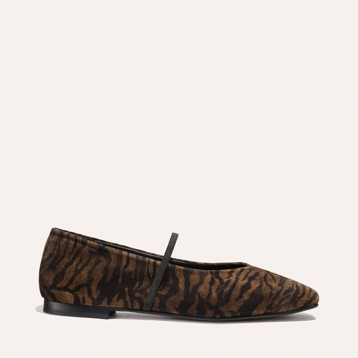 The Phoebe - Brown Zebra Suede by Margaux is a flat shoe featuring a brown and black zebra pattern, a black elastic front strap, and a low black sole, shown against a plain light background.
