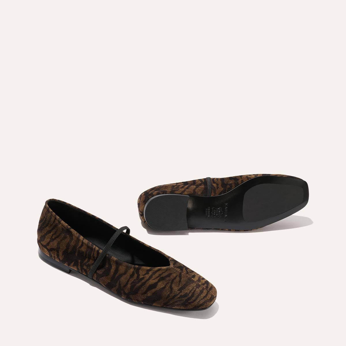 The Phoebe - Brown Zebra Suede flats by Margaux are displayed against a light background, with one shoe upright and the other on its side to reveal the sole, showcasing their stylish brown and black zebra print design.
