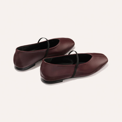 The Phoebe - Burgundy Nappa by margaux-development: burgundy ballet flats with black elastic straps, sacchetto construction for flexible comfort, rounded toe, and flat heel, shown on a plain light background.