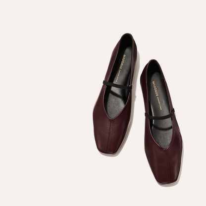 The Phoebe - Burgundy Nappa by margaux-development: burgundy leather flats with black straps and square toes, crafted with sacchetto construction, displayed on a light beige background.
