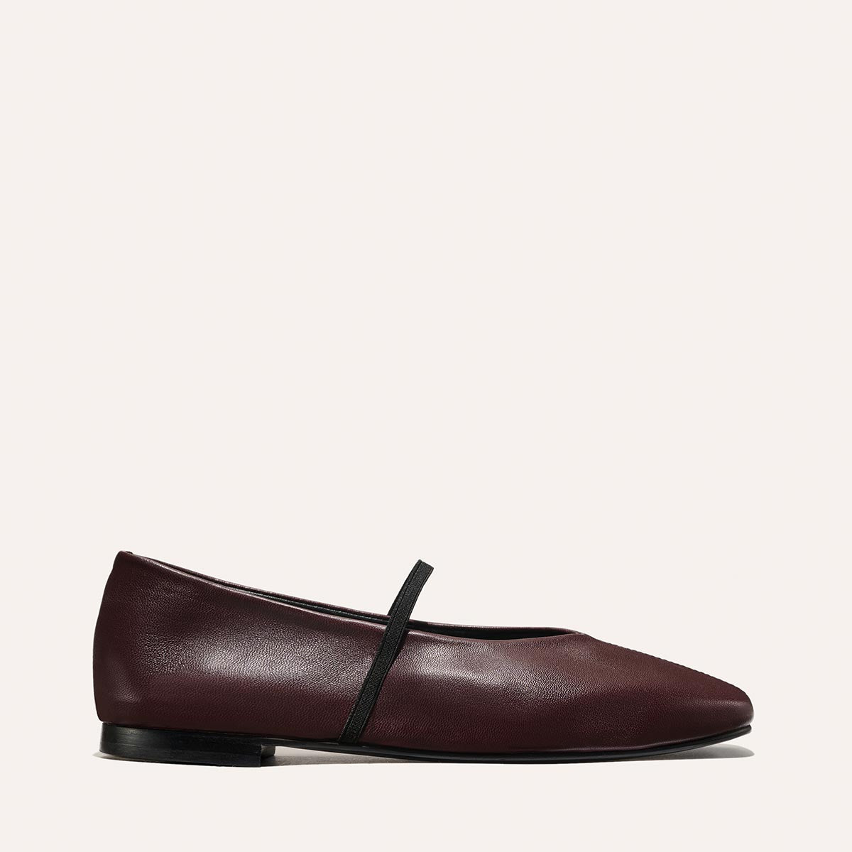 The Phoebe - Burgundy Nappa by margaux-development: a single burgundy flat with a rounded toe, black elastic strap across the top, and low black heel, displayed on a plain light background.