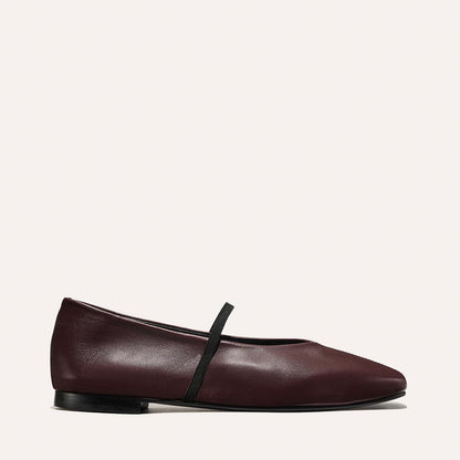 The Phoebe - Burgundy Nappa by margaux-development: a single burgundy flat with a rounded toe, black elastic strap across the top, and low black heel, displayed on a plain light background.