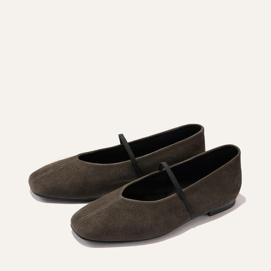 A pair of The Phoebe ballet flats in graphite suede by Margaux, featuring black straps over the top and shown on a light background. Expertly handmade using sacchetto construction, these shoes promise exceptional comfort and elegance.