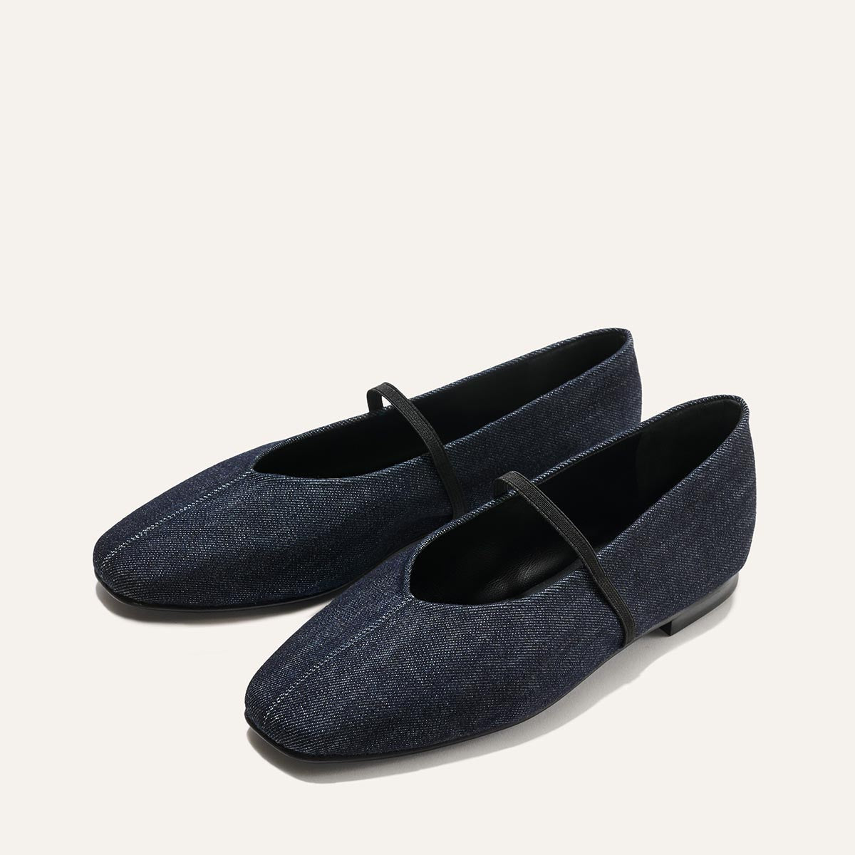 The Phoebe - Indigo Denim by margaux-development features dark blue denim Mary Jane flats with black soles, a single black strap, and a square toe—crafted with sacchetto construction for exceptional softness.