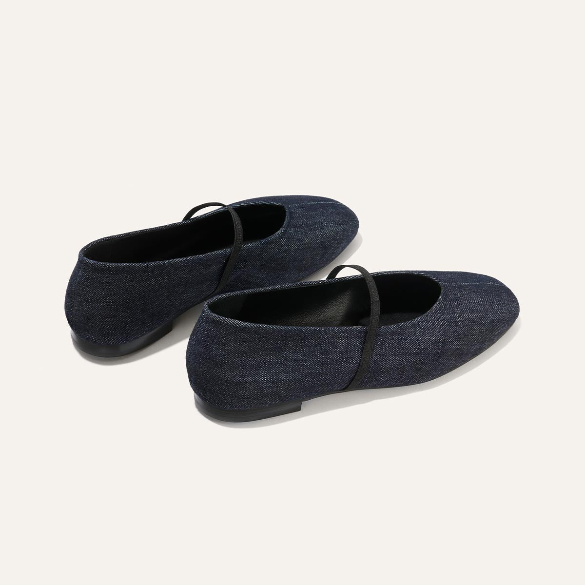 The Phoebe - Indigo Denim by margaux-development: dark blue denim ballet flats with sacchetto construction and thin black elastic straps, shown from the back and side against a light background.