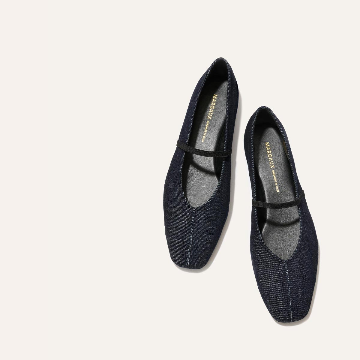 The Phoebe - Indigo Denim by margaux-development: dark denim ballet flats with black soles and a slim black strap, crafted in soft sacchetto construction, shown on a light beige background.