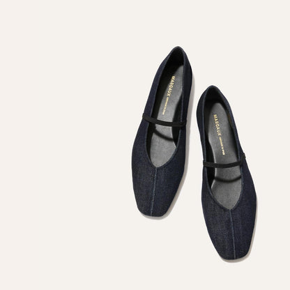 The Phoebe - Indigo Denim by margaux-development: dark denim ballet flats with black soles and a slim black strap, crafted in soft sacchetto construction, shown on a light beige background.