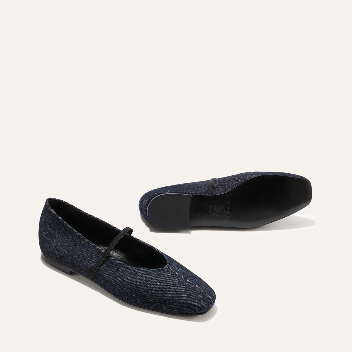 The Phoebe - Indigo Denim by margaux-development features dark denim ballet flats with black soles, a slim strap, and sacchetto construction for comfort. One flat stands upright while the other rests on its side against a light background.