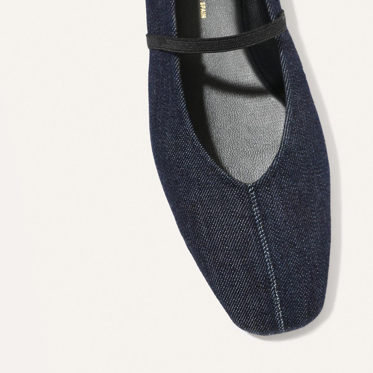 A top view of The Phoebe - Indigo Denim by margaux-development shows a deconstructed dark blue denim flat with a black instep strap, set against a plain white background.