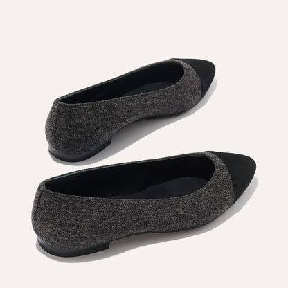 A pair of The Pointe - Grey Flannel flats by margaux-development, featuring dark gray textured fabric, solid black toe caps, and a sleek silhouette, displayed on a light background.