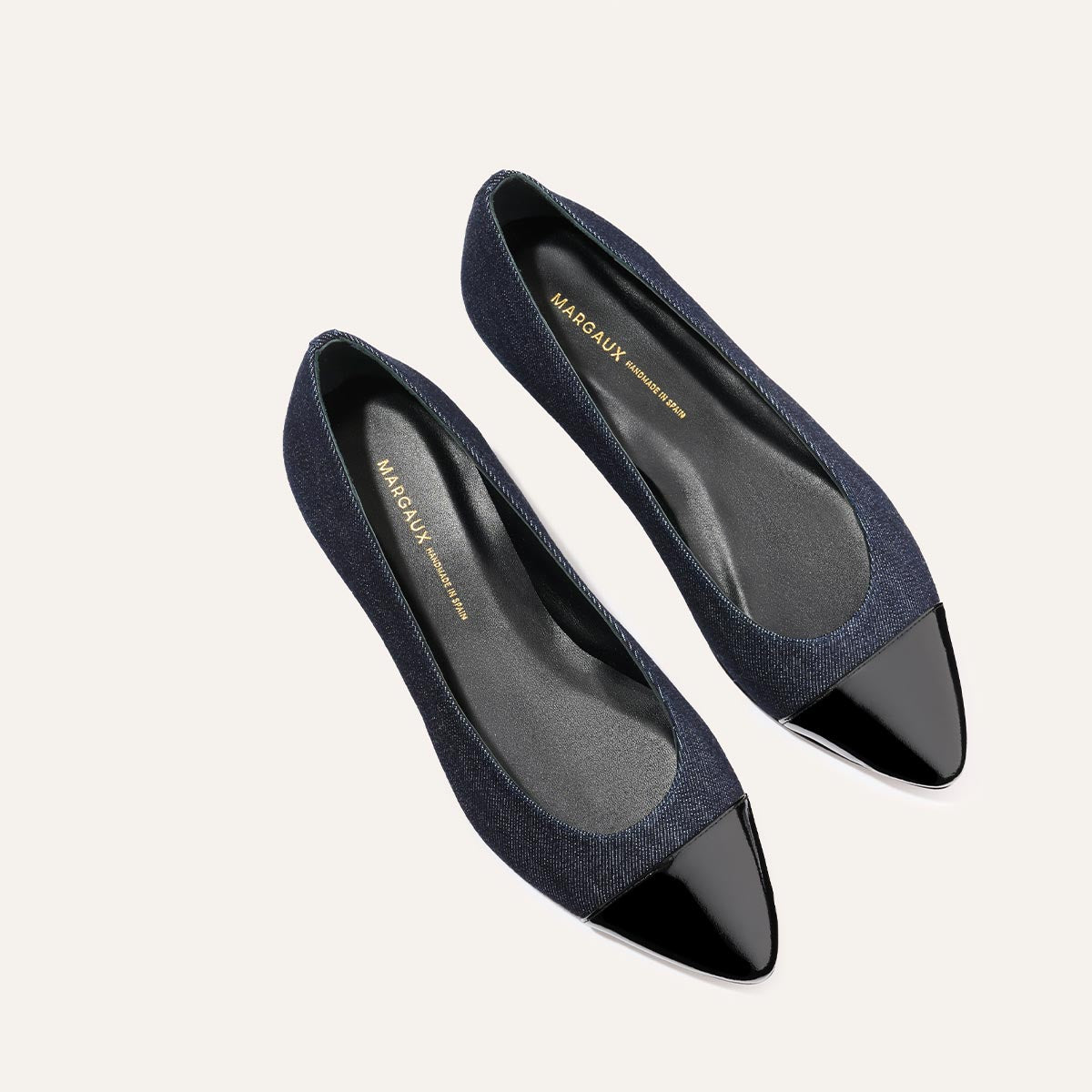 The Pointe - Indigo Denim and Patent by margaux-development features dark denim uppers, glossy black pointed toe caps, a sleek silhouette, and black insoles with gold branding, all shown from above on a light background.