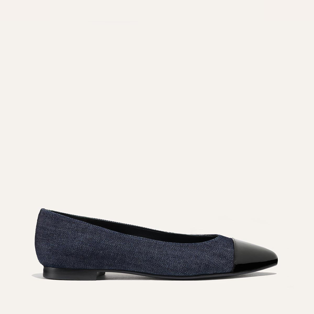 The Pointe by margaux-development is a dark blue indigo denim flat with a sleek silhouette, black patent cap toe, and low heel, shown on a plain light background in a side view.