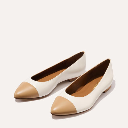 Margaux’s The Pointe in Ivory and Toffee Nappa are women’s flats with a white body, tan pointed toe caps, and low heels, offering a sleek silhouette—displayed on a plain light background.