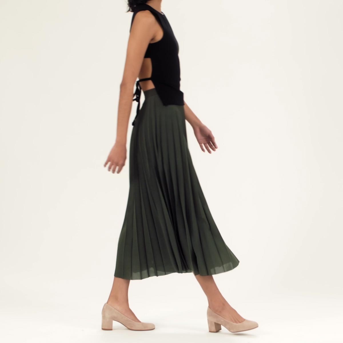 The Heel in Fawn Suede shown on model styled with a green pleated midi skirt and black sleeveless top with an open back.