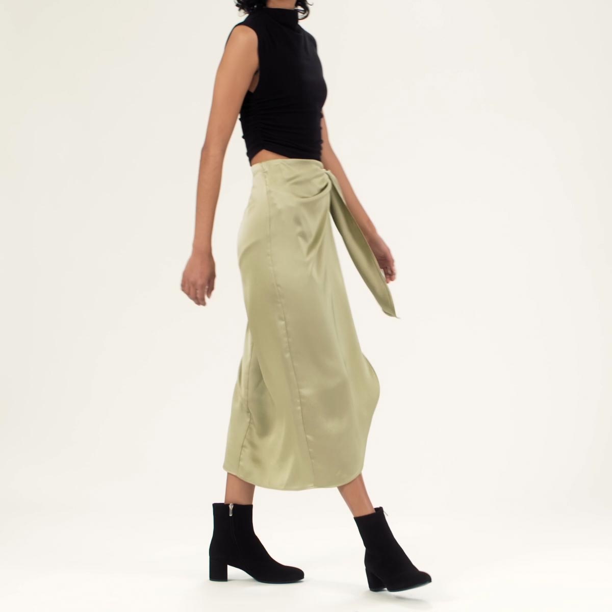 The Boot in Black Suede shown on model styled with a light green silk midi skirt and a sleeveless mock neck top in black.