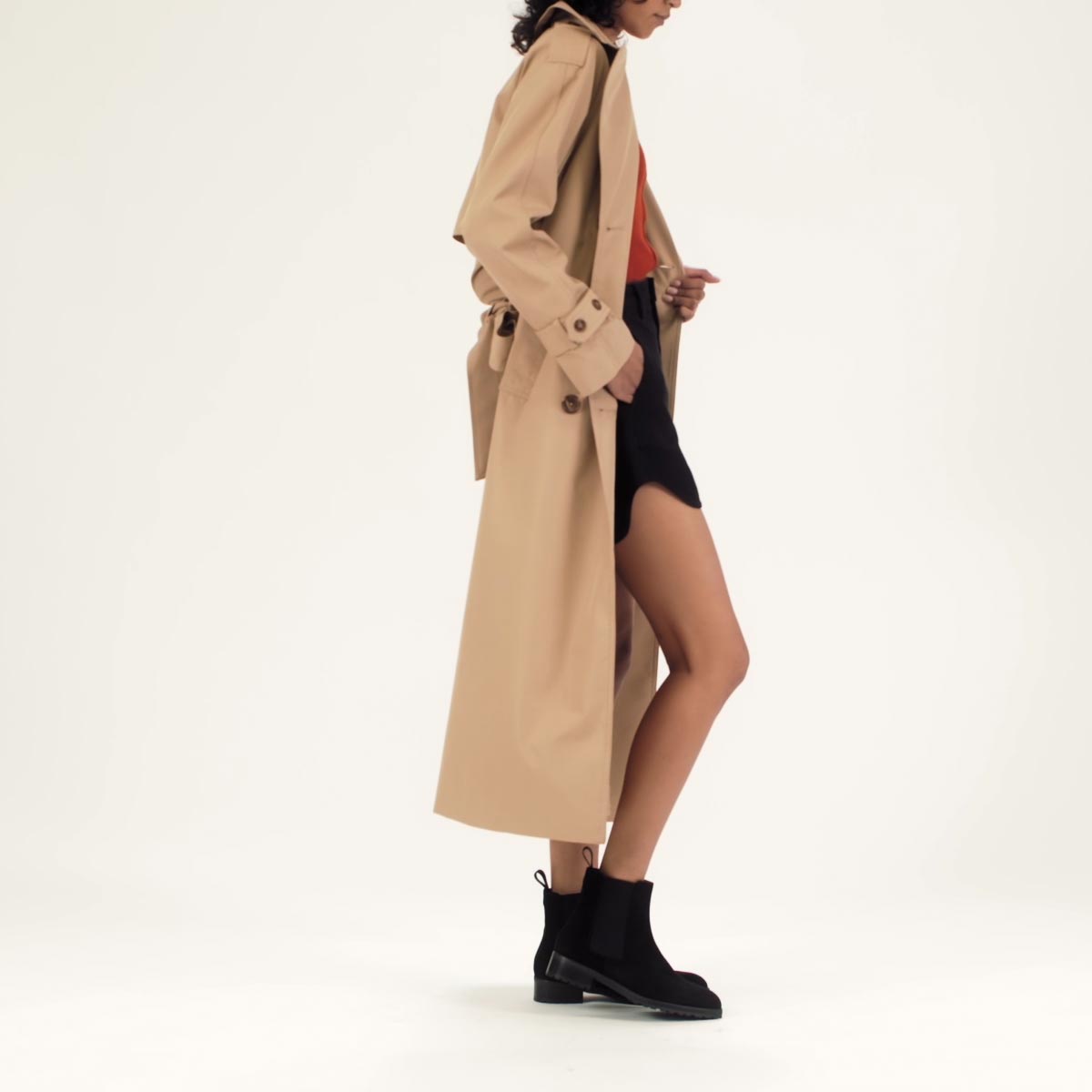 The Chelsea Boot in Black Suede shown on model styled with a tan calf-length trench coat, black mini skirt and red top.