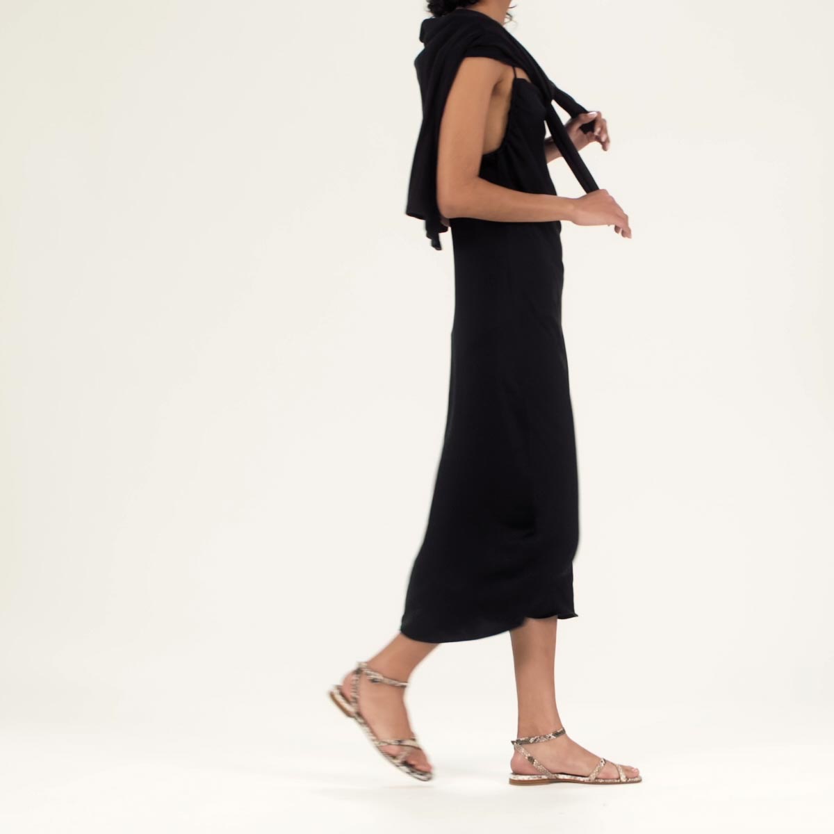 The Flat Sandal in Python Embossed shown on model styled with a black midi dress and a black sweater tied over the shoulders.