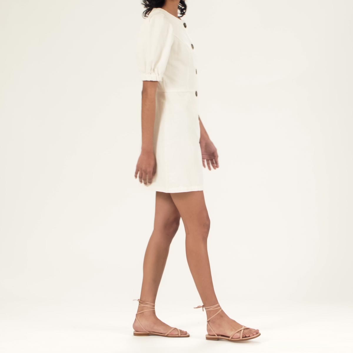 The Wrap Sandal in Rose Nappa shown on model styled with a short white puff-sleeve dress with button details down the front.