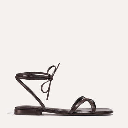 The Wrap Sandal - Espresso Nappa by Margaux is a minimalist dark brown sandal with thin straps, including an ankle-tie bow and toe strap, perfect for versatile summer looks. Displayed on a light background.