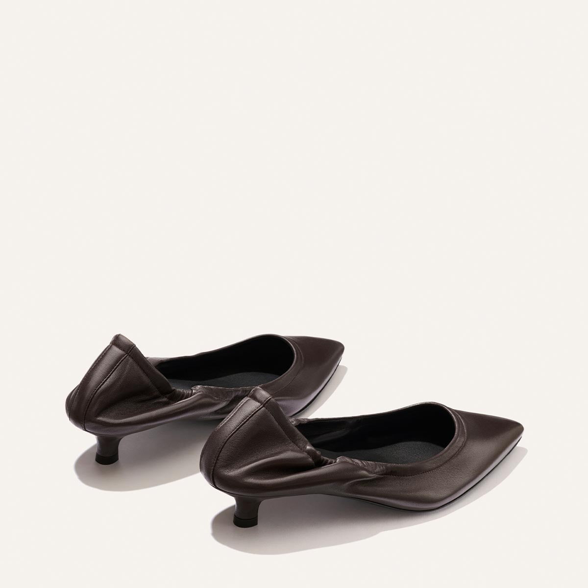 A pair of The Roma 40 - Espresso Nappa pointed-toe flat shoes by Margaux, featuring gathered detailing at the back and a chic heel, is displayed against a plain light background.
