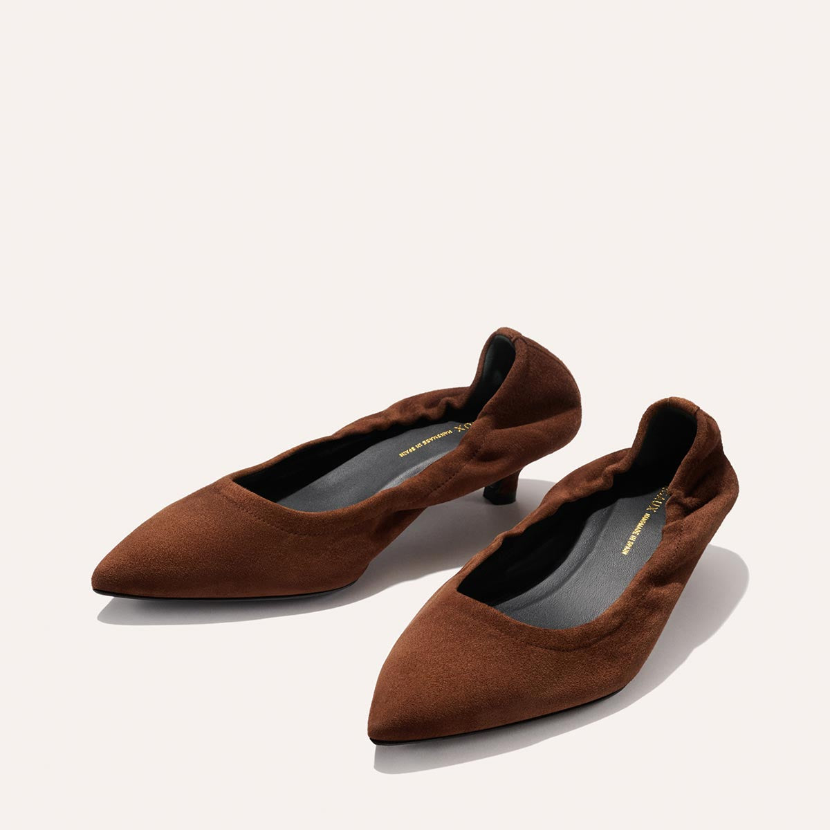 The Margaux The Roma 40 - Ganache Suede heels feature chic low heels, pointed toes, and slightly ruched edges in brown suede, displayed on a light background.