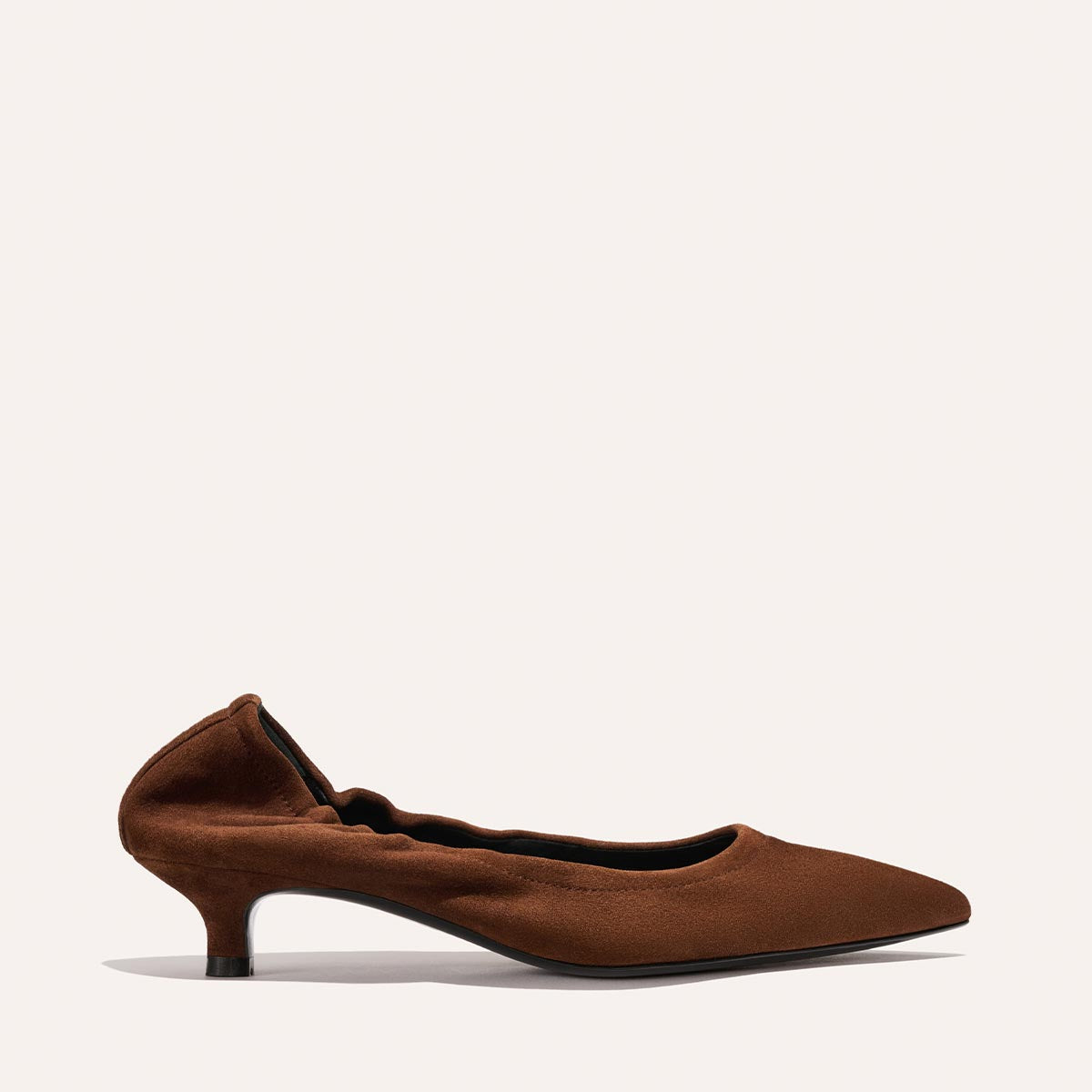 The Roma 40 - Ganache Suede by Margaux is a chic brown suede heel with a pointed toe and softly gathered edges, elegantly showcased on a plain light background.
