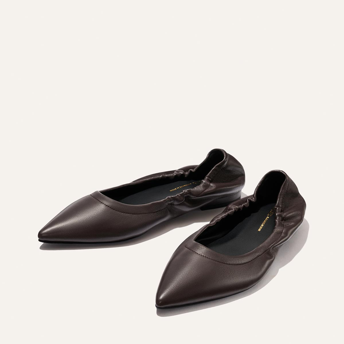 A pair of The Roma - Espresso Nappa pointed-toe ballet flats by Margaux, featuring ruched elastic backs in dark brown leather, are displayed on a light background, exemplifying a refined blend of comfort and sophistication.